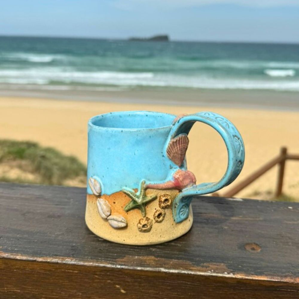 Decorative mug with beach design on a wooden surface with ocean view